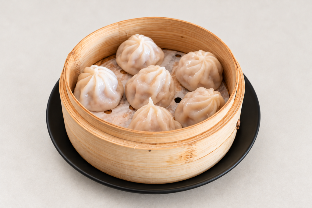 Pork soup dumplings in a bamboo steamer on a light warm gray background at IN RAMEN