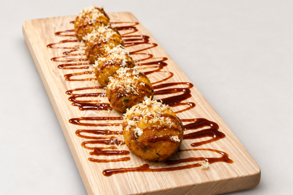 Takoyaki in a single row on a wooden platter with savory sauce and bonito flakes at IN RAMEN